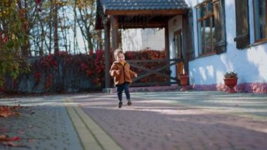 Sevimli, mutlu, yolda koşan küçük çocuk. Güzel gülümseyen çocuk kameraya yaklaşıyor. Düşük açı görünümü.