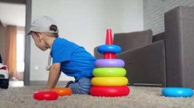 Şapkalı beyaz çocuk oyuncak piramidinin yanında oturuyor. Gülümseyen çocuk ışığı açmak için koşar. Düşük açı görünümü.