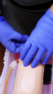 İğneyle yapılan pratik bir işlem. Öğrenci eğitim merkezinde kuklanın eline iğne batırma alıştırması yapıyor. Üst Manzara. Yakın plan. Dikey video