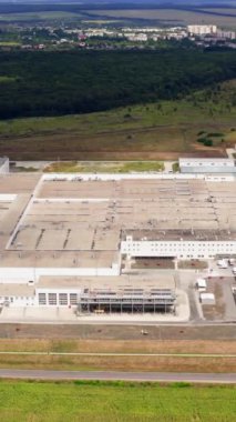 Doğadaki büyük sanayi bölgesi. Araba parkı olan modern bir fabrika. Kırsalda büyük bir imalat. Hava görüntüsü. Dikey video