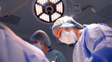 Maskeli ve şapkalı kadın doktor ameliyathanede çalışmaya odaklanmış. Cerrahın ameliyat yaparken düşük açılı görüntüsü.