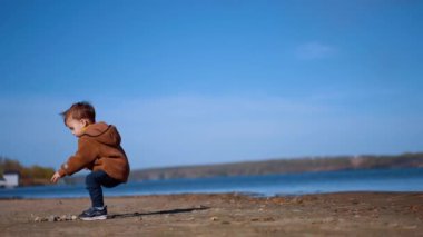 Kafkasyalı bir çocuk yerde bir taş yığınının yanına geldi. Çocuk bir taş aldı ve atmak için suya koştu. Düşük açı görünümü.