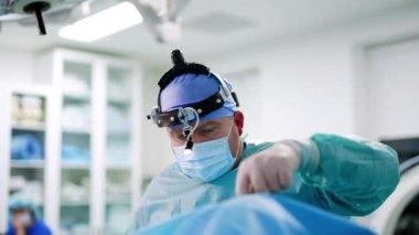 Hastayı ameliyat eden profesyonel bir otolarolog. Kulaklık lambalı doktor enstrüman kullanır. Bulanık arkaplan.