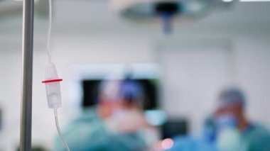 Plastik atık deposunun yarısı tuzlu solüsyonla dolu. Kapatın. Arkaplanda ameliyat yapan cerrahların bulanık görüntüsü.