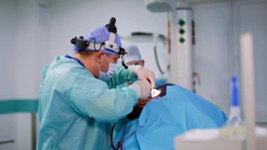 Cerrah, hastanın burun boşluğuna tüplü bir alet sokuyor. Laringolojik ameliyatta bir erkek doktorun yan görüntüsü..