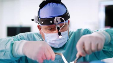 Ameliyatı farlı, kendine güvenen erkek cerrah yürütür. Doktor gırtlak işleminde metal aletler kullanıyor. Kapat..