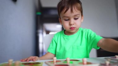 Açık yeşil tişörtlü, masada sakince oynayan ciddi bir bebek. Yeni yürümeye başlayan çocuk bulmaca çözüyor. Kapatın. Bulanık arkaplan.
