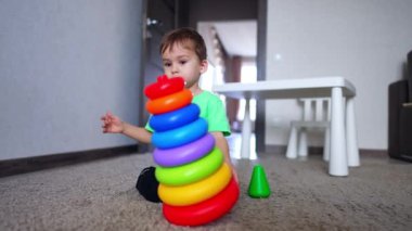 Oyuncak piramidi yere iten ve parçalara ayıran güzel çocuk. Beyaz çocuk evde oynuyor..