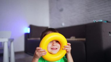 Tatlı bebek oyuncak piramidin sarı halkasına bakıyor. Çocuk kameraya gülümserken kafasına koyuyor. Düşük açı görünümü.