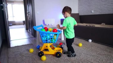 Tatlı çocuk oyuncak alışveriş arabasındaki renkli toplara dokunuyor. Neşeli bebek mutlu bir şekilde dönüyor.