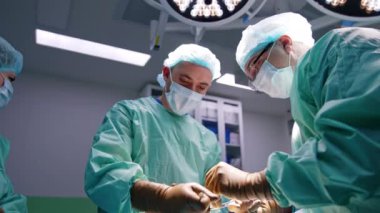 Erkek cerrahlar ortopedi cerrahisinde işbirliği yaparlar. Travma ameliyatına odaklanan doktorlara düşük açılı bakış açısı. Bayan hemşire aletleri hazırlıyor..