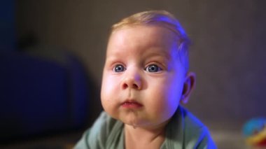 Büyük mavi gözleri ve tombul yanakları olan sarışın bir bebeğin sevimli yüzü. Kapatın. Bebek şaşkınlıkla önümüze bakıyor. Bulanık arkaplan.