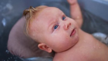 Suda hareket eden büyük mavi gözlü beyaz bir bebek. Banyo yapan sevimli bir çocuk. Kapat..