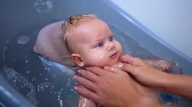 Tanınmayan bir anne tatlı bebeğini yıkıyor. Küçük çocuk banyo yaparken el sallıyor. Kapat..