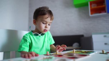 Sevimli küçük erkek bebek masasında oturup oyuncaklarına dikkatle bakıyor. Çocuk gerekli parçacığı almak için elini uzatıyor..