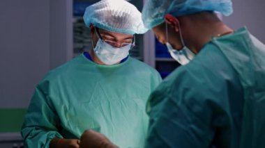 Maskeli, şapkalı ve gözlüklü yetişkin bir erkek cerraha yaklaşıyoruz. Ameliyathanede çalışan bir doktorun portresi..