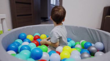 Kuru havuzda oturan sevimli gülümseyen çocuk. Bebek çocuk renkli topları koridora fırlatıyor..
