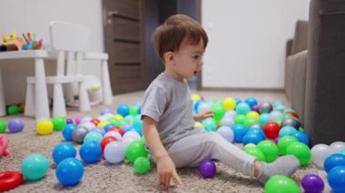 İki yaşında bir çocuk renkli topların arasında yerde oturuyordu. Çocuk yeşil topu aldı ve ileri attı..