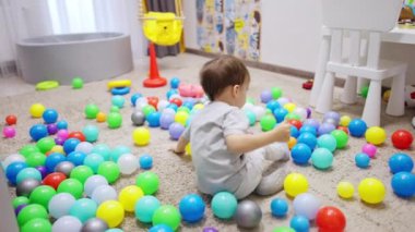 Şirin çocuk yere dağılmış topların arasında oturuyor. Bebekler topların üzerine uzanır ve yuvarlanırlar..