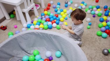 Koyu saçlı küçük çocuk kuru havuzun yanında oturuyor. Güzel bebek çıkartmayla oynuyor. Üst görünüm.