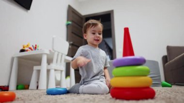 Gülen çocuk piramidin tabanına renkli halkalar takıyor. Odasında oyuncaklarla oynayan mutlu beyaz çocuk. Düşük açı görünümü.