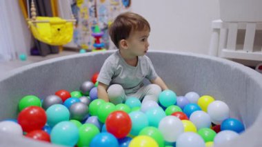 Sakin bebek kuru havuzda hayaların içinde oturur. Bebek toplara uzanıyor ve havuzda rahatlıyor..