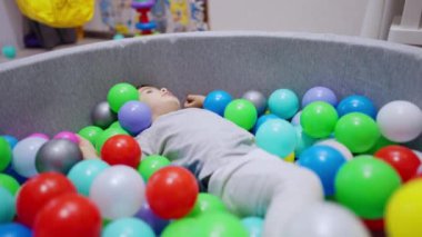 Kuru havuzda yatan bebek dik oturur. Sevimli çocuk topu ileri atıyor. Bulanık arkaplan.