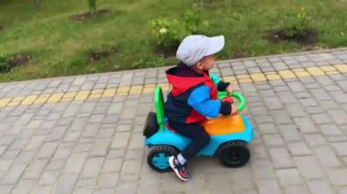 Sevimli çocuk parkın etrafında mutlu bir şekilde at sürüyor. Şapkalı çocuk oyuncak araba kullanıyor. Üst görünüm.