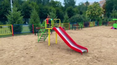 Tatlı çocuk merdivenlerden yukarı kayıyor. Küçük çocuk üste oturur, ayaklarını yere vurur ve aşağı iner..