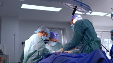 Bir grup doktor ameliyat masasının etrafında duruyor. Beyin cerrahları modern ameliyathanede mikro cerrahi yapıyorlar. Düşük açı görünümü.