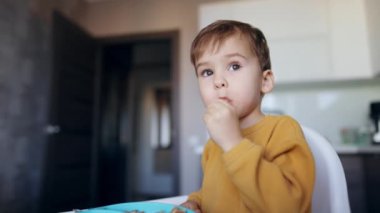 Masada oturan küçük çocuk yemeğini yiyor. Bebek bir kaşık alır ve başının üstüne kaldırır..