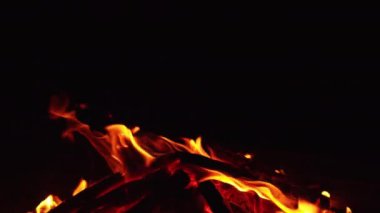 Kamp ateşinde odun yakmak. Sola doğru hareket eden küçük alevlerle şenlik ateşi yakıyor. Kapatın. Siyah arkaplan.