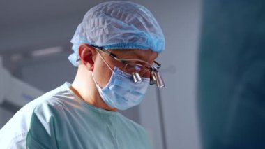 İş yerinde cihaz gözlüğü takan kendinden emin bir erkek cerrah. Doktor elinde metal bir alet tutuyor..