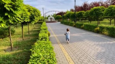 Kot pantolonlu küçük çocuk kameradan uzak duruyor. Küçük çocuk yazın yeşil parkta topla koşuyor..