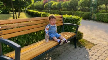 Parktaki bankta oturan Kafkasyalı çocuk. Çocuk banktan şişeyi alır ve içmeye başlar..