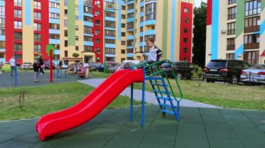 Gülümseyen çocuk merdiveni tırmanır. Mutlu bebek aşağı kayıyor ve oyun parkına koşuyor.