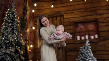 Sevimli bebeğini sallayan şefkatli bir anne. Anne oğluyla ahşap kulübede oynuyor. Arkaplanda Noel ağaçları.