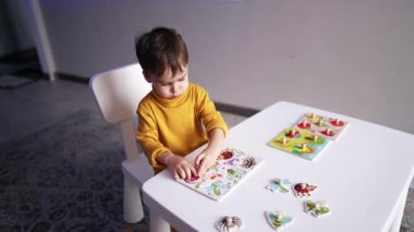 Sevimli küçük çocuk masada oturup böceklerle bulmaca topluyor. Bebek oyun yoluyla nesneleri öğreniyor. Üst görünüm.