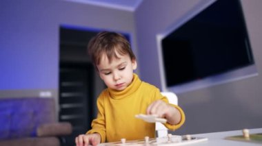 Sarı kazaklı sevimli küçük çocuk yapboz oyununa odaklanmış. Bebek evde oynuyor ve ders çalışıyor..
