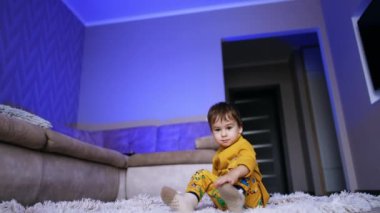 Koyu saçlı erkek bebek halının üzerinde oturuyor. Çocuk ekoseyle yatar ve yuvarlanır..