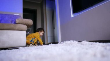 Sarı elbiseli enerjik beyaz çocuk neşeyle zıplıyor ve yerde yuvarlanıyor. Çocuk evde eğleniyor. Düşük açı görünümü.