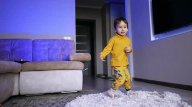 Neşeli çocuk enerjik bir şekilde adımını atıyor ve dönüyor. Mutlu çocuk ekose kumaşın üstüne düşüp yuvarlanıyor. Düşük açı görünümü.