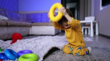 Sarı kazaklı sevimli kahverengi saçlı bebek oyuncak yüzüğü kafasına takıyor. Evde oynayan komik çocuk..
