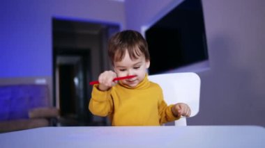 Sarı kazak giyen sevimli çocuk masa başı çizim yapıyor. Çocuğun elinde kırmızı bir keçeli kalem var..