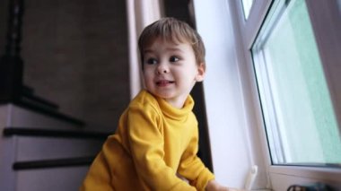 Pencerenin yanında duran güzel çocuk. Gülümseyen çocuk geriye bakıyor ve zıplıyor. Düşük açı görünümü.