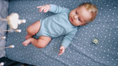 Güzel, tombul sarışın erkek bebek beşiğinde uyanık yatıyor. Sevimli çocuk bebek karyolasına bakıyor. Üst görünüm.