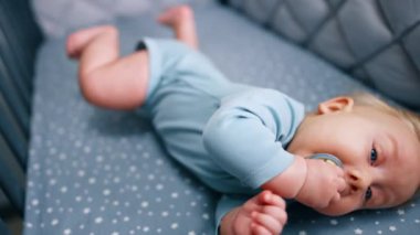 Karyolasında sevimli minik bir çocuk. Sevimli bebek ağzında bir emzik tutuyor ve yana yuvarlanıyor. Kapat..