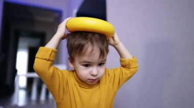 Sarı kazaklı güzel esmer erkek çocuk oyuncaklarla oynuyor. Bebek oyuncak piramidin yüzüğünü kafasına yerleştiriyor ve bırakıyor. Kapat..