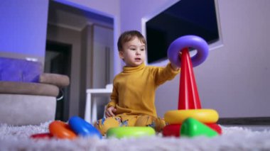 Piramitle oynayan tatlı sakin bir çocuk. Çocuk yerde oturup oyuncak monte ediyor. Düşük açı görünümü.