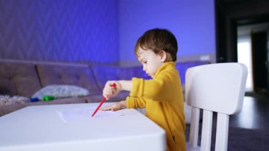 Tatlı beyaz oğlan resim çizmeye odaklanmış. Çocuk kaleme kalem kapağı koymaya çalışıyor ama başarısız oluyor..